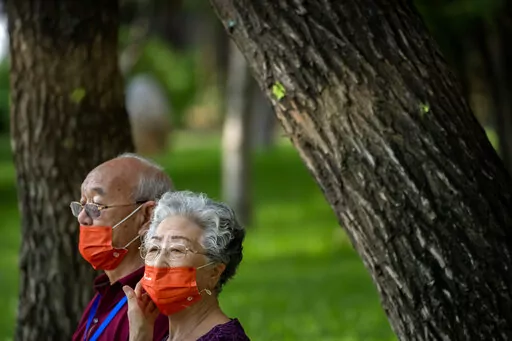 People wearing face masks sit on a bench at a public park in Beijing, Friday, July 8, 2022. The Chinese capital Beijing appears to have backed off a plan to launch a vaccine mandate for entry into certain public spaces after pushback from residents. (AP Photo/Mark Schiefelbein)