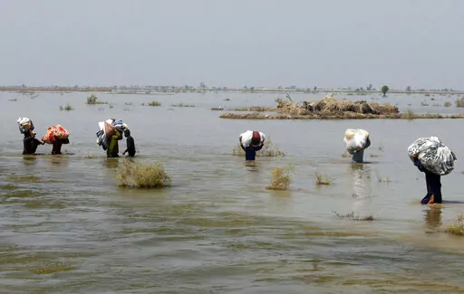 Victims of heavy flooding from monsoon rains crowd carry relief aid through flood water in the Qambar Shahdadkot district of Sindh Province, Pakistan, Sept. 9, 2022. The United Nations says weather disasters costing $200 million a day and irreversible climate catastrophe looming show the world is “heading in the wrong direction.” (AP Photo/Fareed Khan, File)