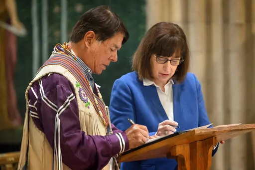 In this image provided by Cornell University, Ray Halbritter, left, representing the Oneida Indian Nation, and Cornell University President Martha E. Pollack, sign documents that repatriate ancestral remains from the university to the Oneida Indian Nation during a ceremony in Sage Chapel, Tuesday, Feb, 21, 2023, in Ithaca, NY. Cornell University has returned ancestral remains to the Oneida Indian Nation that were inadvertently dug up in 1964 and stored for decades in a school archive. (Jason Kos