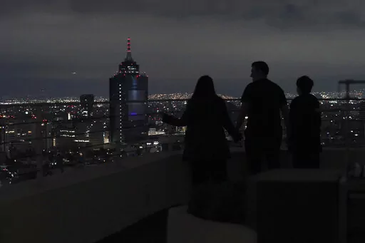 A family looks out at Mexico City from their apartment building rooftop after an earthquake early Thursday, Sept. 22, 2022. The magnitude 6.8 quake struck at 1:19 a.m. local time, causing at least two deaths, damaging buildings and setting off landslides near the epicenter in the western state of Michoacan. (AP Photo/Marco Ugarte)