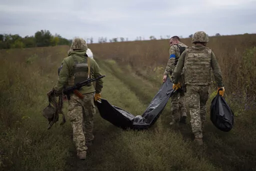 Ukrainian servicemen carry a bag containing the body of a Ukrainian soldier, center, as one of them, right, carries the remains of a body of a Russian soldier in a retaken area near the border with Russia in Kharkiv region, Ukraine, Saturday, Sept. 17, 2022. (AP Photo/Leo Correa)