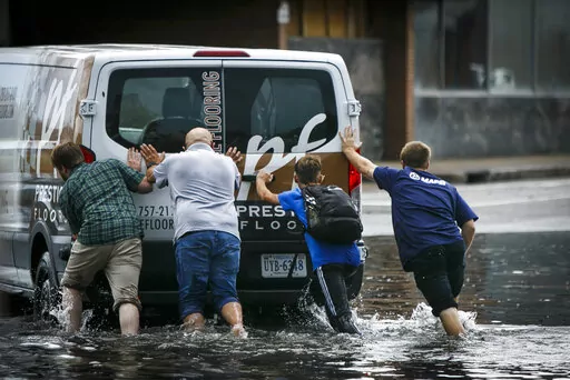 A stalled vehicle is pushed from flood waters following a rainstorm in Norfolk, Va., on Thursday, Aug. 6, 2020. The increasing threat of sea-level rise on Virginia’s coast means that an afternoon rainstorm can strand drivers for hours and damage cars beyond repair. The city of Norfolk is trying to do something about that. Officials have partnered with the tech firm FloodMapp and the Waze traffic app to warn residents of flooded roadways in real time. (Kristen Zeis/The Virginian-Pilot via AP)