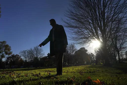 Cook County, Ill., Sheriff's Commander Jason Moran, who leads the sheriff's missing persons initiative stands in silhouette and points to a round cylinder that marks a grave of a person who self-identified as Seven, at the Mount Olivet Cemetery on Chicago's Far South Side Monday, Nov. 13, 2023. “That’s a horrible circumstance that someone could die and no one knows who they are. That’s why we pursue these cases so strongly, out of dignity,” says Moran, who oversees the sheriff’s missin