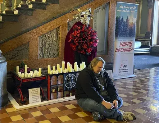 A man prays in Latin in front of a display installed by Satanic Temple Iowa at the Iowa State Capitol in Des Moines, Iowa, on Tuesday, Dec. 12, 2023. A Mississippi man accused of destroying a statue of the pagan idol Baphomet at Iowa's state Capitol pleaded guilty Friday to a reduced charge in return for prosecutors dropping a felony hate crime count. (Caleb McCullough/The Gazette via AP, file)