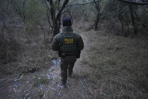 A border patrol agent walks along a trail littered with bracelets used by human smuggling groups near the Rio Grande at the U.S.-Mexico border, Thursday, Feb. 13, 2025, in McAllen, Texas. (AP Photo/Eric Gay)