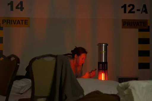 A woman looks at her mobile phone in a hotel underground parking turned into a bomb shelter during an air raid alert in Kyiv, Ukraine, Sunday, Feb. 27, 2022. Terrified men, women and children sought safety inside and underground, and the government maintained a 39-hour curfew to keep people off the streets as more than 150,000 Ukrainians fled to neighboring countries and the United Nations warned the number could grow to 4 million if fighting escalates.(AP Photo/Vadim Ghirda)