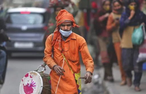 A man wears his face mask below his nose and walks in a market area with a traditional percussion instrument in Jammu, India, Saturday, Jan.15, 2022. It’s mandatory to wear a mask in India. And police are out on the streets, watching people to make sure they are in place. People caught without wearing a mask are fined. Some local governments, like the one in the capital New Delhi, have recruited new staff to ensure the rules are followed.c(AP Photo/Channi Anand)