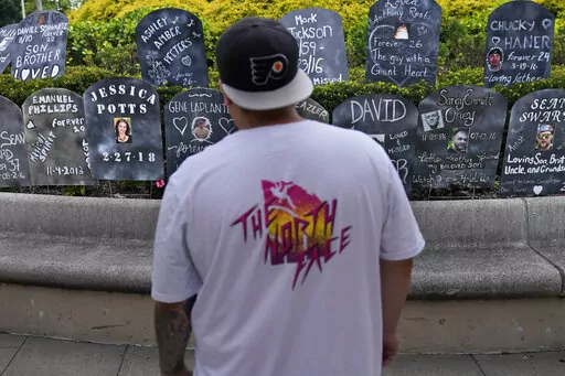 A man looks at cardboard gravestones with the names of victims of opioid abuse outside the courthouse where the Purdue Pharma bankruptcy is taking place in White Plains, N.Y., Monday, Aug. 9, 2021.  A federal appeals panel is scheduled to hear arguments on whether members of the Sackler family can be granted protection from lawsuits as part of a bankruptcy settlement for the company they own, OxyContin maker Purdue Pharma. If the company doesn’t get what it wants, it could have to fight off th