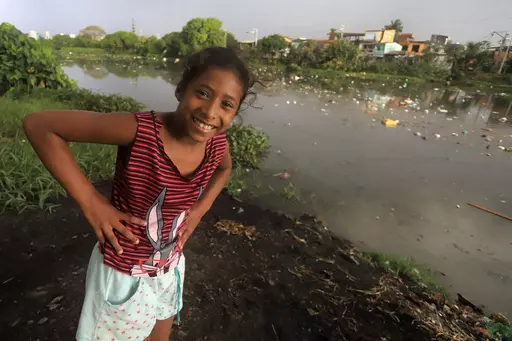A girl smiles while eyeing the camera as she stands alongside the Sao Joaquim canal, its banks and water littered with garbage, in the Barreiro neighborhood of Belem, Brazil, Wednesday, Aug. 9, 2023. According to the Instituto Trata Brasil, specializing in research of basic sanitation and water protection, the city of Belem, host of the Amazon Summit, has one of the worst sanitation rates in Brazil, with a sewage system available to only 17.1 % of the population. (AP Photo/Paulo Santos)