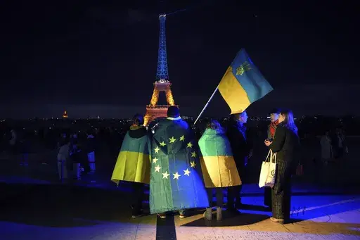Ukrainians hold Ukrainian and European flag as the Eiffel Tower is illuminated with the colors of Ukraine to mark the third anniversary of Russia's invasion of the country, in Paris, Monday, Feb. 24, 2025. (AP Photo/Christophe Ena, file)