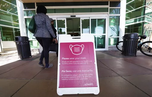 A sign advising visitors to don face coverings stands outside the main entrance to UCHealth University of Colorado hospital Friday, April 1, 2022, in Aurora, Colo.  COVID cases are starting to rise again in the United States, with numbers up in most states and up steeply in several. One expert says he expects more of a “bump” than the monstrous surge of the first omicron wave, but another says it’s unclear how high the curve will rise and it may be more like a hill.  (AP Photo/David Zalubo
