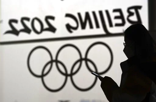 A woman looks at her phone as she passes an Olympic logo inside the main media center for the 2022 Winter Olympics, Jan. 18, 2022, in Beijing. (AP Photo/David J. Phillip, File)
