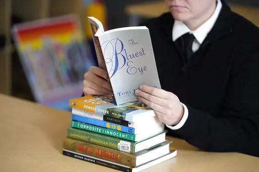 Amanda Darrow, director of youth, family and education programs at the Utah Pride Center, poses with books, including "The Bluest Eye," by Toni Morrison, that have been the subject of complaints from parents in Salt Lake City on Dec. 16, 2021. The wave of book bannings around the country has reached a level not seen for decades. (AP Photo/Rick Bowmer, File)