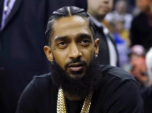 Rapper Nipsey Hussle attends an NBA basketball game between the Golden State Warriors and the Milwaukee Bucks in Oakland, Calif., March 29, 2018. Three years after rapper Hussle was gunned down outside a Los Angeles clothing store that he founded to help revitalize the neighborhood where he grew up, a trial will finally begin Wednesday, June 15, 2022, for the man charged with killing him. (AP Photo/Marcio Jose Sanchez, File)