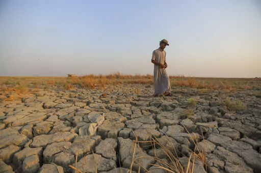 A fisherman walks across a dry patch of land in the marshes of southern Iraq which has suffered dire consequences from back to back drought and rising salinity levels, in Dhi Qar province, Iraq, Friday Sept. 2, 2022. (AP Photo/Anmar Khalil)