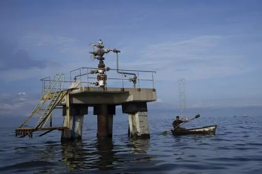 A fisherman navigates past an inoperative oil drill on Lake Maracaibo in Venezuela, early Oct. 12, 2022.A 49-page indictment unsealed on Oct. 20 in New York federal court has charged seven individuals with conspiring to smuggle oil from PDVSA, purchase sensitive U.S. military technology, and launder tens of millions of dollars on behalf of wealthy Russian businessmen. (AP Photo/Ariana Cubillos, File)