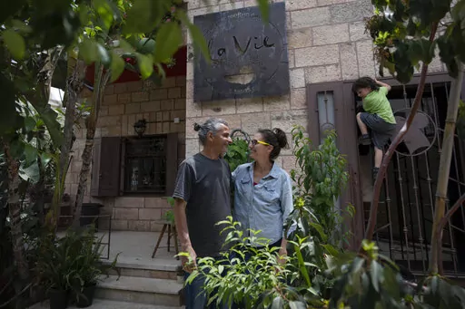 Kenae Totah, 5, right, plays while his parents Morgan Cooper, 41, center and Saleh Totah, right, pose for a photo in front of their restaurant, at the West Bank city of Ramallah, Monday, May 2, 2022.  The Israeli military body in charge of civilian affairs in the occupied West Bank has developed a new policy that would heavily regulate entry into the territory. Critics say it extends Israel's nearly 55-year military rule even further into every corner of Palestinian society. It would impose new 