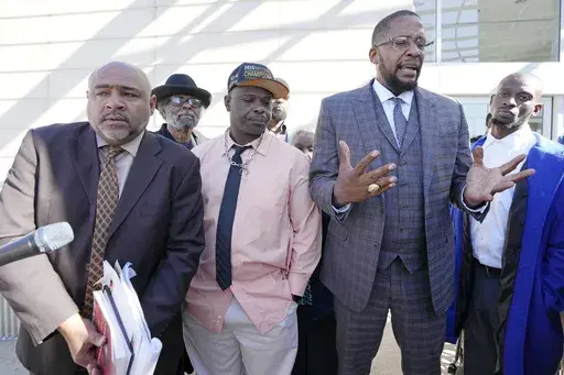 Lead civil attorney Malik Shabazz, second from right, speaks to reporters while his clients, Michael Corey Jenkins, right, and Eddie Terrell Parker, second from left, stand with their local attorney Trent Walker, outside the federal courthouse in Jackson, Miss., Tuesday, March 19, 2024, following the sentencing of the second of six former Mississippi Rankin County law enforcement officers who committed numerous acts of racially motivated, violent torture on Parker and Jenkins in 2023. (AP Photo/
