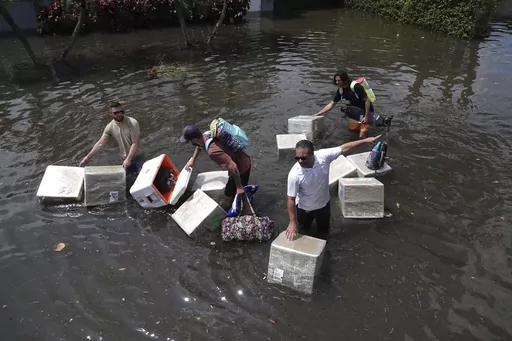 People try and save valuables as they wade through flood waters in the Edgewood neighborhood of Fort Lauderdale, Fla., April 13, 2023. Over 25 inches of rain fell in South Florida since Monday, causing widespread flooding. (Joe Cavaretta/South Florida Sun-Sentinel via AP)