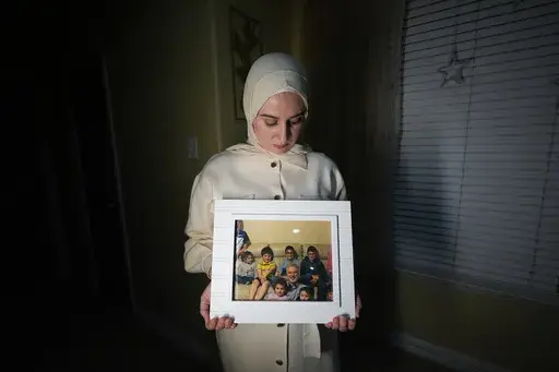 Maryam Kamalmaz hold a photo of her father with some of his 14 grandchildren in Grand Prairie, Texas, Jan. 17, 2024. U.S. officials have developed specific and highly credible intelligence suggesting that Majd Kamalmaz, an American citizen who disappeared seven years ago while traveling in Syria has died, Maryam Kamalmaz said Saturday, May 18. (AP Photo/Julio Cortez, File)