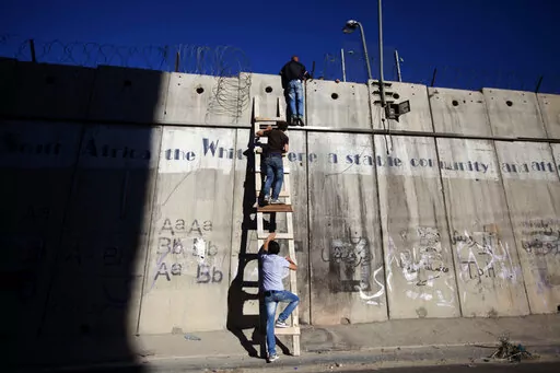 Palestinians use a ladder to climb over the separation barrier with Israel on their way to pray at the al-Aqsa Mosque in Jerusalem during the Muslim holy month of Ramadan, in Al-Ram, north of Jerusalem, July 11, 2014. Israel on Monday, Jan. 31, 2022, called on Amnesty International not to publish an upcoming report accusing it of apartheid, saying the conclusions of the London-based international human rights group are “false, biased and antisemitic.” (AP Photo/Majdi Mohammed, File)