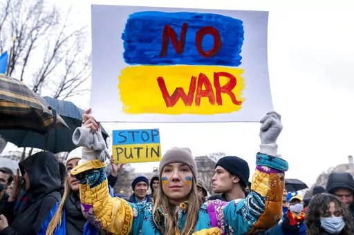 A tear rolls down through the colors of the Ukrainian flag on the cheek of Ukranian Oleksandra Yashan of Arlington, Va., as she becomes emotional while holding a sign that reads "No War" during a vigil to protest the Russian invasion of Ukraine in Lafayette Park in front of the White House in Washington, Thursday, Feb. 24, 2022. (AP Photo/Andrew Harnik)
