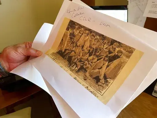 In this July 8, 2021, photo, adjunct history professor and research associate Larry Larrichio holds a copy of a late 19th century photograph of pupils at an Indigenous boarding school in Santa Fe during an interview in Albuquerque, N.M.  A new federal report on the legacy of boarding schools for Native Americans underscores how closely the U.S. government collaborated with churches to Christianize the Indigenous population as part of a project to sever them from their culture, their identities a