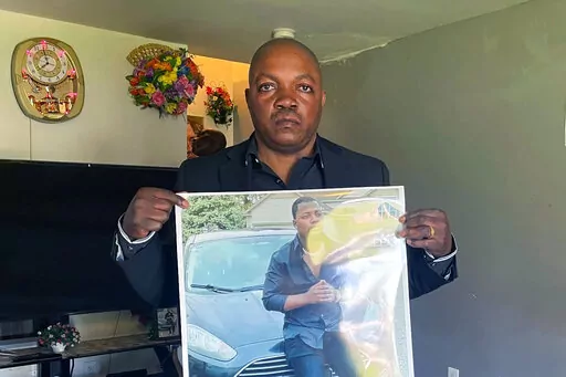 Peter Lyoya holds up a picture of his son Patrick Lyoya, 26, in his home in Lansing, Mich., April 14, 2022. Patrick was face-down on the ground when he was fatally shot in the head by a Grand Rapids Police officer after resisting arrest on April 4, 2022. Grand Rapids police released four videos from different sources Wednesday, nine days after Patrick Lyoya was killed during a traffic stop. Prominent civil rights attorney Ben Crump and Lyoya's family are planning to hold a news conference Thursd