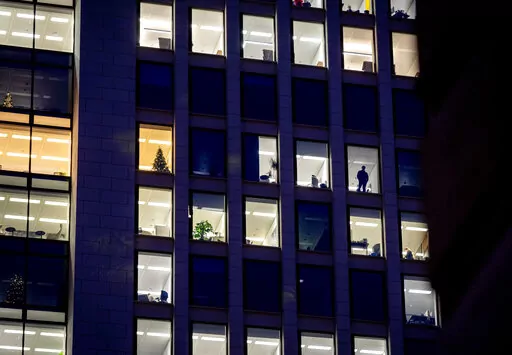 A man looks out of the window of an office building in Frankfurt, Germany, Dec. 6, 2022. A new report says climate commitments by companies aren’t always as green as they seem. The report published Monday, Feb. 13, 2023, concludes that major brands are exaggerating how ambitious their efforts to cut greenhouse gas emissions are, essentially misleading consumers, investors and governments. (AP Photo/Michael Probst, File)