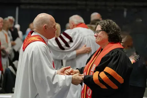In this photo provided by the United Methodists of Eastern Pennsylvania, Rev. Dr. Beth Stroud, right, holds hands with Bishop John Schol after offering a prayer of blessing at the Wildwoods Convention Center, Wildwood, N.J., on Tuesday, May 21, 2024, as he prepares to retire in August. Twenty years ago, Stroud was defrocked as a pastor after telling her congregation that she was in a committed same-sex relationship. On Tuesday night, less than three weeks after the UMC repealed its anti-LGBTQ ba