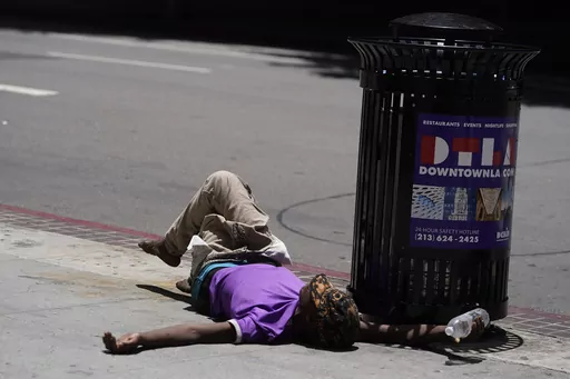 A homeless person lies on the sidewalk while holding a water bottle, Sunday, July 2, 2023, in downtown Los Angeles. Excessive heat warnings remain in place in many areas across the U.S. and are expected to last at least through Monday. (AP Photo/Damian Dovarganes, File)