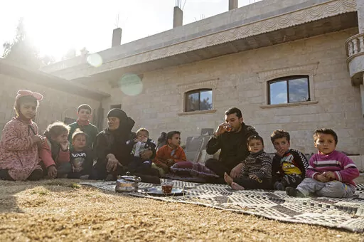 Milhem Daher, 35, drinks tea as he sits with his family outside his house in the village of Kasrat Srour, in the southeastern countryside of the Raqqa province, Syria, Monday, Feb. 7, 2022. Raqqa, the former de facto capital of the self-proclaimed IS caliphate and home to about 300,000, is now free, but many of its residents try to leave. Those with capital are selling their property to save up for the journey to Turkey. Those without money struggle to get by. (AP Photo/Baderkhan Ahmad)