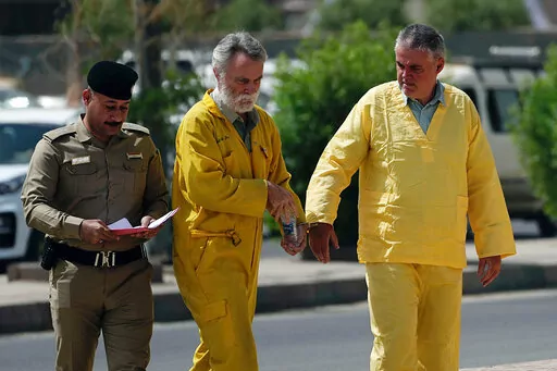 Volker Waldmann, right, and Jim Fitton, center, are handcuffed as they walk to a courtroom in Baghdad, Iraq, Sunday, May 22, 2022. Waldmann and Fitton, accused of smuggling ancient shards out of Iraq, appeared in a Baghdad court Sunday, telling judges they had not acted with criminal intent and had no idea they might have broken local laws. (AP Photo/Hadi Mizban)