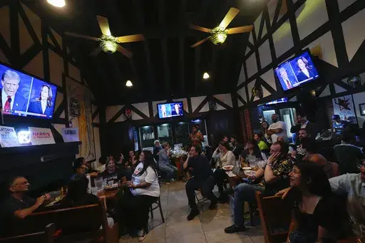 People watch TV screens showing a debate between Democratic presidential nominee Vice President Kamala Harris, right on screen, and Republican presidential nominee former President Donald Trump, at Sports Grill Kendall, where the Miami-Dade Democratic Hispanic Caucus had organized a watch party, Tuesday, Sept. 10, 2024, in Miami. (AP Photo/Rebecca Blackwell, File)