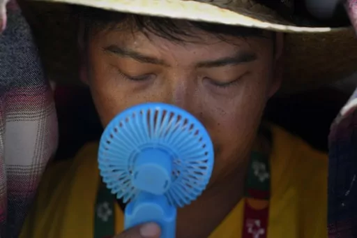 A World Youth Day volunteer uses a small fan to cool off from the intense heat, as he waits ahead of the Pope Francis arrival at Passeio Marítimo in Algés, just outside Lisbon, Aug. 6, 2023. UN weather agency says Earth sweltered through the hottest summer ever as record heat in August capped a brutal, deadly three months in northern hemisphere. (AP Photo/Armando Franca, File)