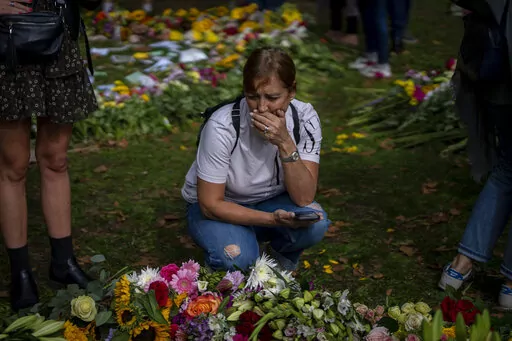 A woman reacts next to flowers and messages for Queen Elizabeth II at the Green Park memorial, near Buckingham Palace, in London, Sept. 10, 2022. Because she reigned and lived for so long, Queen Elizabeth II's death was a reminder that mortality and the march of time are inexorable. (AP Photo/Emilio Morenatti, File)