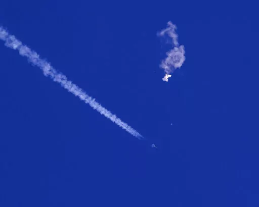 In this photo provided by Chad Fish, the remnants of a large balloon drift above the Atlantic Ocean, just off the coast of South Carolina, with a fighter jet and its contrail seen below it, Saturday, Feb. 4, 2023. The downing of the suspected Chinese spy balloon by a missile from an F-22 fighter jet created a spectacle over one of the state’s tourism hubs and drew crowds reacting with a mixture of bewildered gazing, distress and cheering. (Chad Fish via AP)