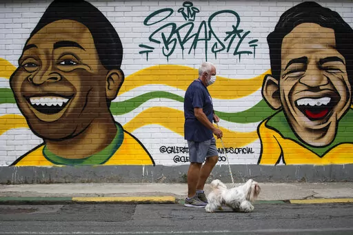 A man walks his dog past a mural of Brazilian soccer stars Pele, left, and Garrincha in Rio de Janerio, Brazil, Friday, Dec. 30, 2022. Edson Arantes do Nascimento, known to the world as Pele, died in Sao Paulo Thursday at the age of 82. (AP Photo/Bruna Prado)