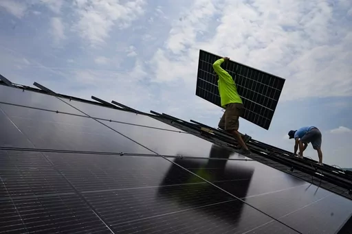 Nicholas Hartnett, owner of Pure Power Solar, carries a panel as he and Brian Hoeppner, right, install a solar array on the roof of a home in Frankfort, Ky., Monday, July 17, 2023. Since passage of the Inflation Reduction Act, it has boosted the U.S. transition to renewable energy, accelerated green domestic manufacturing, and made it more affordable for consumers to make climate-friendly purchases, such as installing solar panels on their roofs. (AP Photo/Michael Conroy)