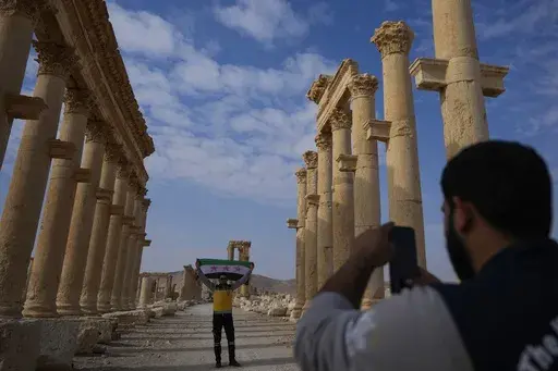 A member of the Syrian Civil Defense (White Helmets) takes a photo of his colleague holding the new Syrian flag at the ancient city of Palmyra, Syria, Saturday, Jan. 25, 2025. (AP Photo/Khalil Hamra)