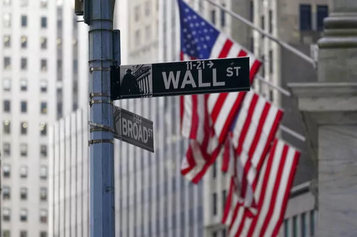 The Wall St. street sign is framed by the American flags flying outside the New York Stock exchange, Friday, Jan. 14, 2022, in the Financial District.  Stocks are off to a mixed start on Wall Street Friday, March 25, wrapping up a bumpy week with more uncertainty about where to go next.  (AP Photo/Mary Altaffer, File)