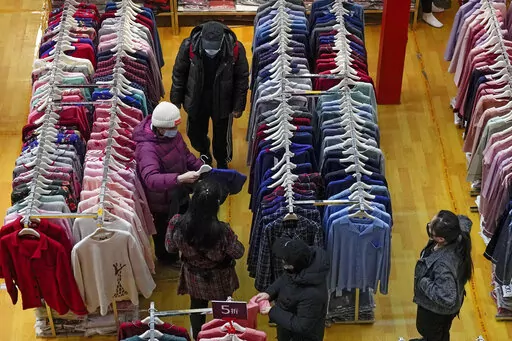 People wearing face masks shop clothing during a promotion New Year sale at a mall in Beijing on Jan. 16, 2022. China’s economic growth edged up to a still-weak 4.8% over a year earlier in the first three months of 2022 as spreading coronavirus outbreaks prompted shutdowns of major industrial cities. (AP Photo/Andy Wong, File)