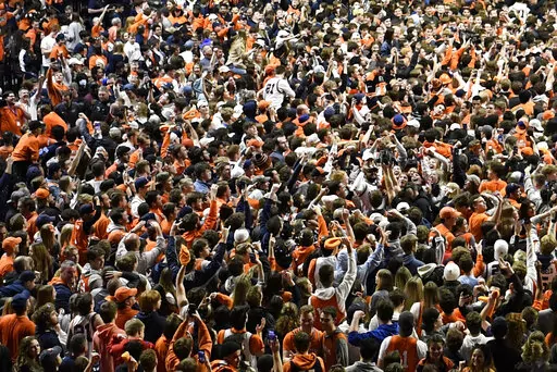 Fans storm the court at the conclusion of a college basketball game in Champaign, Ill., on Sunday, March 6, 2022. After about two months of falling COVID-19 cases, pandemic restrictions have been lifted across the U.S., and many people are taking off their masks and returning to indoor spaces. (AP Photo/Michael Allio)