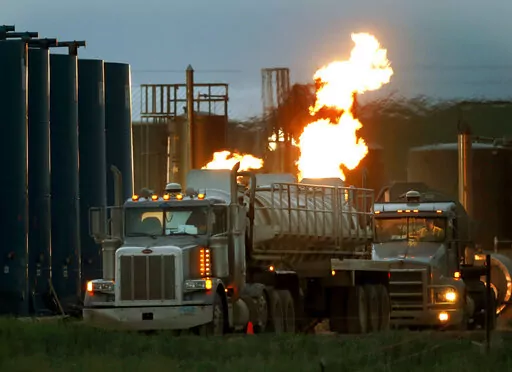 Drivers and their tanker trucks capable of hauling water and hydraulic fracturing liquid line up near a natural gas burn off flame and storage tanks in Williston, N.D., on June 9, 2014. Under new rules proposed by the Securities and Exchange Commission on Monday, March 21, 2022, companies would be required to disclose the greenhouse gas emissions they produce and how climate risk affects their business, as part of a drive across the government to address climate change. (AP Photo/Charles Rex Arb