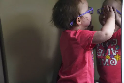 The Hackneys’ daughter looks at her reflection in a bedroom mirror during a supervised visit at her parent's home in Oakdale, Pa., on Thursday, Nov. 17, 2022. At 8 months old, the young child was taken from her parents custody after arriving at the hospital severely dehydrated and malnourished. The Hackneys and their lawyer believe the Allegheny County Family Screening tool may have flagged the couple as dangerous because of their disabilities. (AP Photo/Jessie Wardarski)