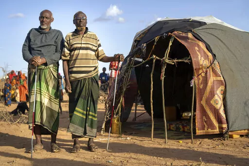 Mohamed Kheir Issack, 80, right, and and Issack Farow Hassan, 75, stand outside Issack's shelter at a camp for displaced people on the outskirts of Dollow, Somalia on Tuesday, Sept. 20, 2022. The two blind men are friends and as close as brothers, gripping each other's hands in their mutual darkness as tightly as they hold their canes. Near the end of their lives, the most alarming drought in more than half a century in Somalia has stripped them of their animals and homes. (AP Photo/Jerome Delay
