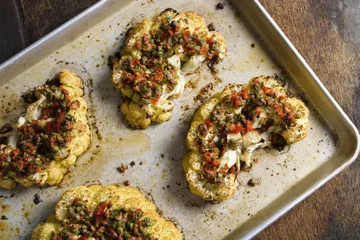 This image released by Milk Street shows a recipe for cauliflower steaks with pickled peppers, capers and parmesan. (Milk Street via AP)