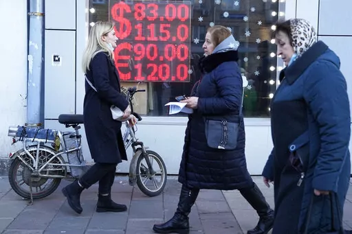 People walk past a currency exchange office screen displaying the exchange rates of U.S. Dollar and Euro to Russian Rubles in Moscow's downtown, Russia, Feb. 28, 2022. Ordinary Russians are facing the prospect of higher prices as Western sanctions over the invasion of Ukraine sent the ruble plummeting. That's led uneasy people to line up at banks and ATMs on Monday in a country that has seen more than one currency disaster in the post-Soviet era. (AP Photo/Pavel Golovkin, File)